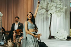 A guest in a light blue lehenga celebrates joyfully with raised arms at an elegant Indian wedding reception.