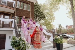 Wedding party dressed in pink outfits and traditional red bridal attire pose together on outdoor stairs.