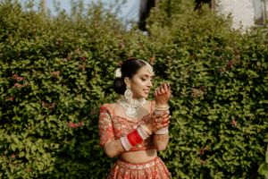 Traditional Indian bridal jewelry and bangles complement an embroidered red lehenga against garden foliage.
