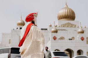 View of a majestic Sikh Gurdwara temple with golden domes and someone in traditional dress in the foreground.