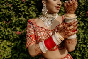 Traditional Indian bridal jewelry and red outfit details with intricate henna designs on hands.