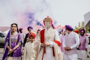 Colorful traditional Sikh wedding celebration with vibrant purple and red attire amid smoke effects outdoors.