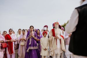 A group wearing traditional Indian wedding attire gathering outdoors with vibrant purple and cream colored clothing.