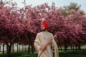 Figure in traditional Indian attire stands before blooming pink cherry blossom trees in spring garden.