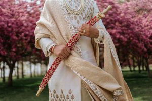 Traditional embroidered white outfit with henna designs photographed in a garden with blooming pink cherry blossoms.