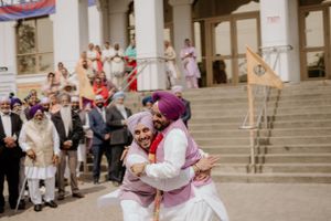 Traditional Sikh celebration with people gathered on stone steps as two figures embrace in bright cultural attire.