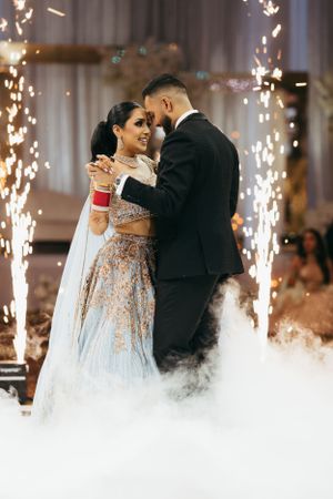 A couple shares their first dance at a fusion wedding with sparklers and fog effects creating a magical atmosphere.