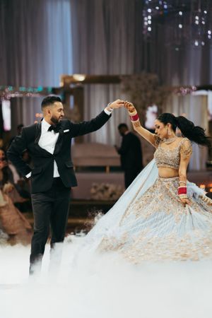 A couple shares a romantic dance moment on their wedding day, with the bride in an elegant cream lehenga and groom in tuxedo.