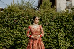 Beautiful red lehenga against lush green garden backdrop in outdoor bridal portrait.