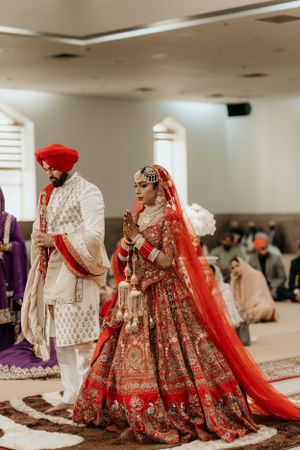 Traditional Indian wedding ceremony with couple in ornate red and white attire including embellished lehenga and sherwani.