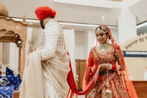 A couple in traditional Indian wedding attire holds hands during their ceremony, with the bride wearing a red lehenga.