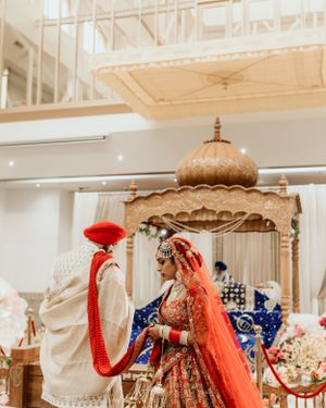 Elegant Indian wedding mandap with golden domed structure and couple in traditional red and cream outfits.