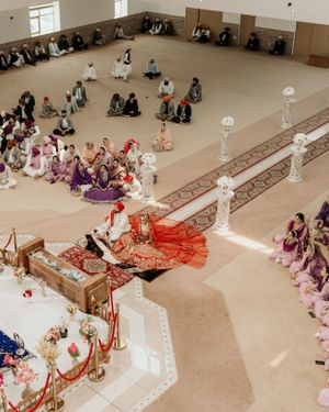 Aerial view of a traditional wedding ceremony in a mosque with guests seated on the floor around ornate decorations.