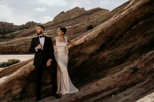 A couple poses elegantly against dramatic red rock formations in formal wedding attire.