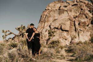 A couple in black attire poses against dramatic rock formations in Joshua Tree National Park at sunset.