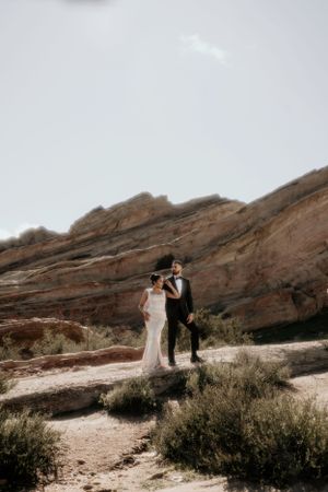 A couple shares an intimate moment against towering desert cliffs in wedding attire.
