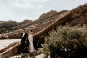 A couple poses for a wedding photo against towering red rock formations in a desert landscape.