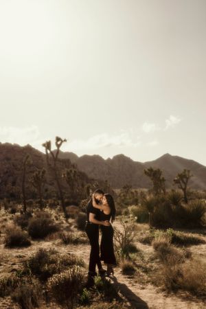 A romantic scene captured in a desert landscape with Joshua trees and mountains at sunset.