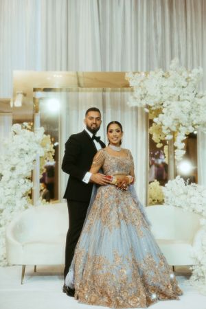 A couple poses in formal attire at an elegant wedding reception with white floral decor and soft lighting.