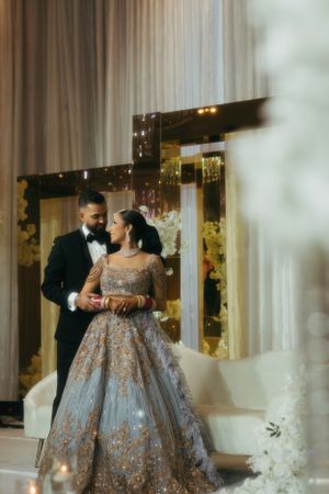 Elegant couple in formal attire share an intimate moment at a wedding reception with floral decor and mirrored backdrop.