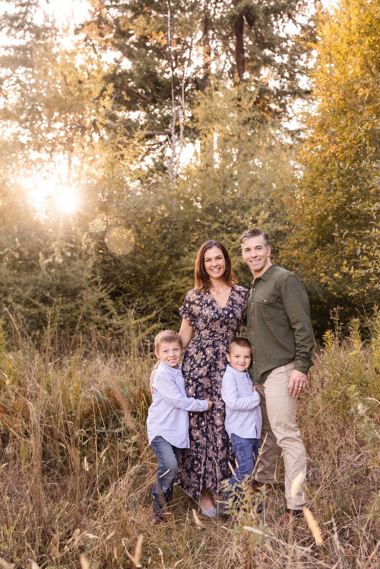 A family poses together in a sunlit autumn field with golden foliage and tall grass during sunset.