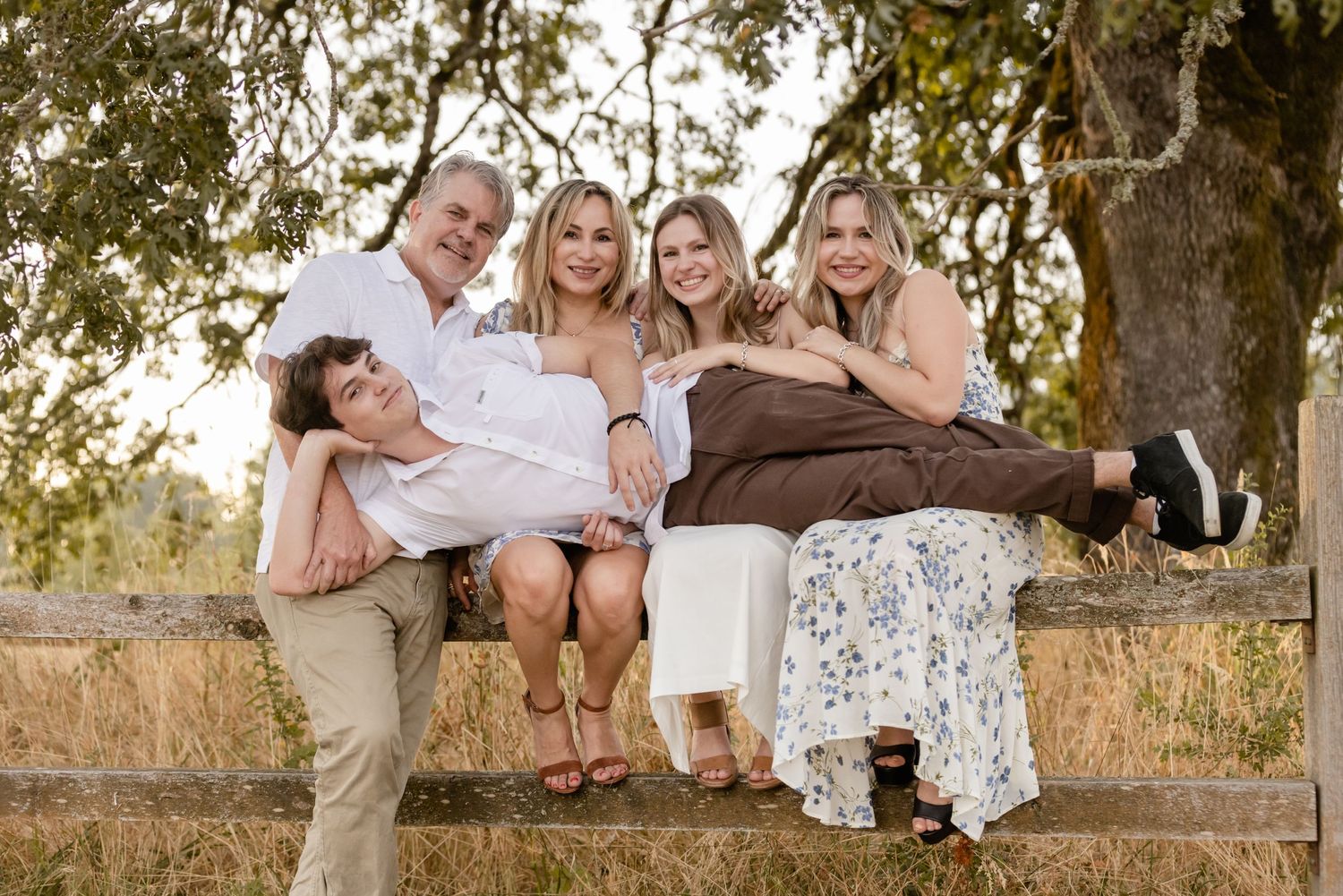 A group sitting together on a rustic wooden fence in a casual outdoor setting during golden hour.