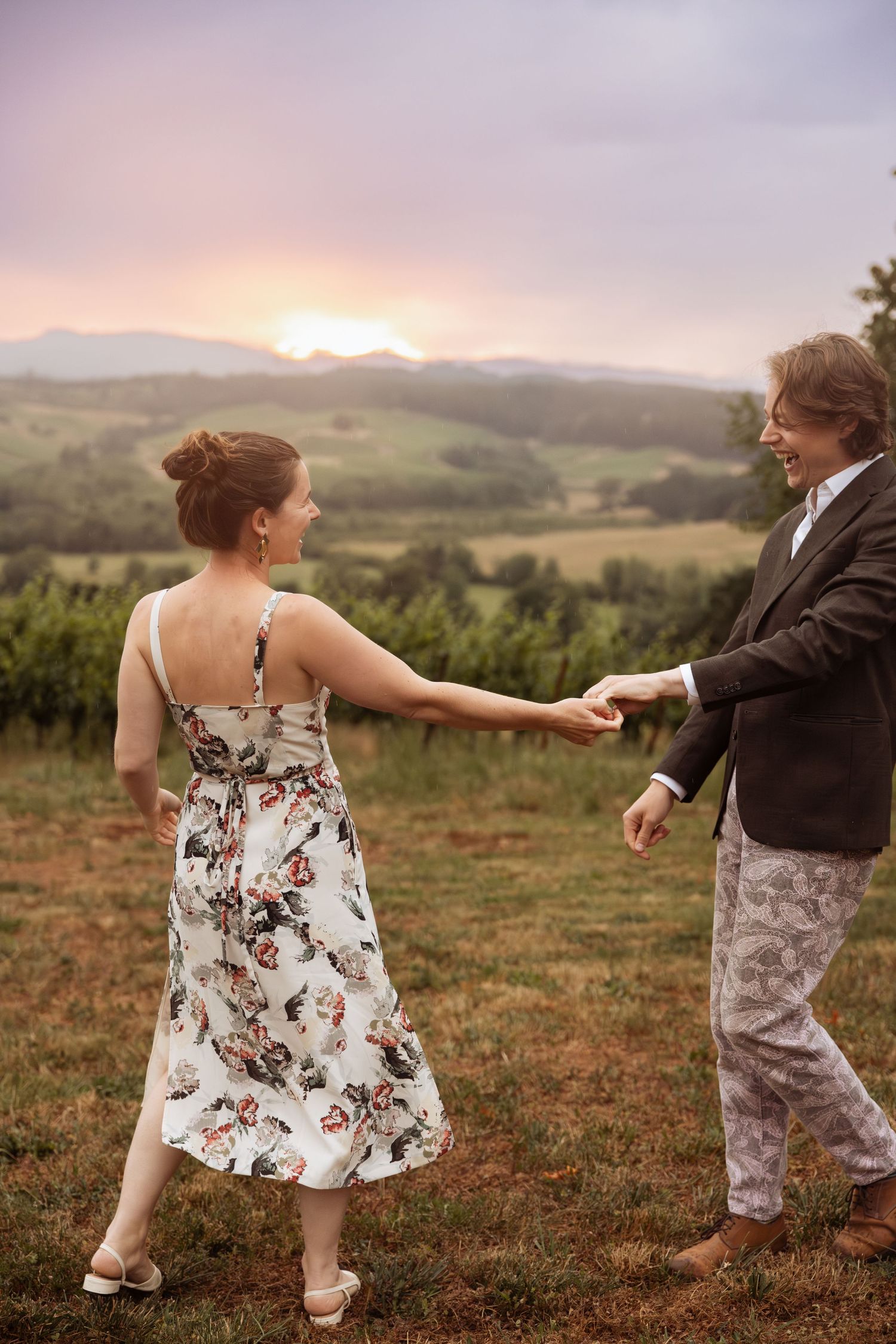 Two people dance together on a hilltop at sunset with rolling countryside views in the background.