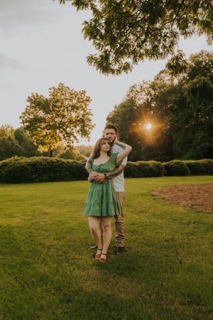 A romantic embrace in a sunlit garden with green hedges and golden hour lighting.