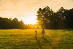 Silhouettes of figures playing in an open grassy field at sunset with golden sunlight streaming through trees.