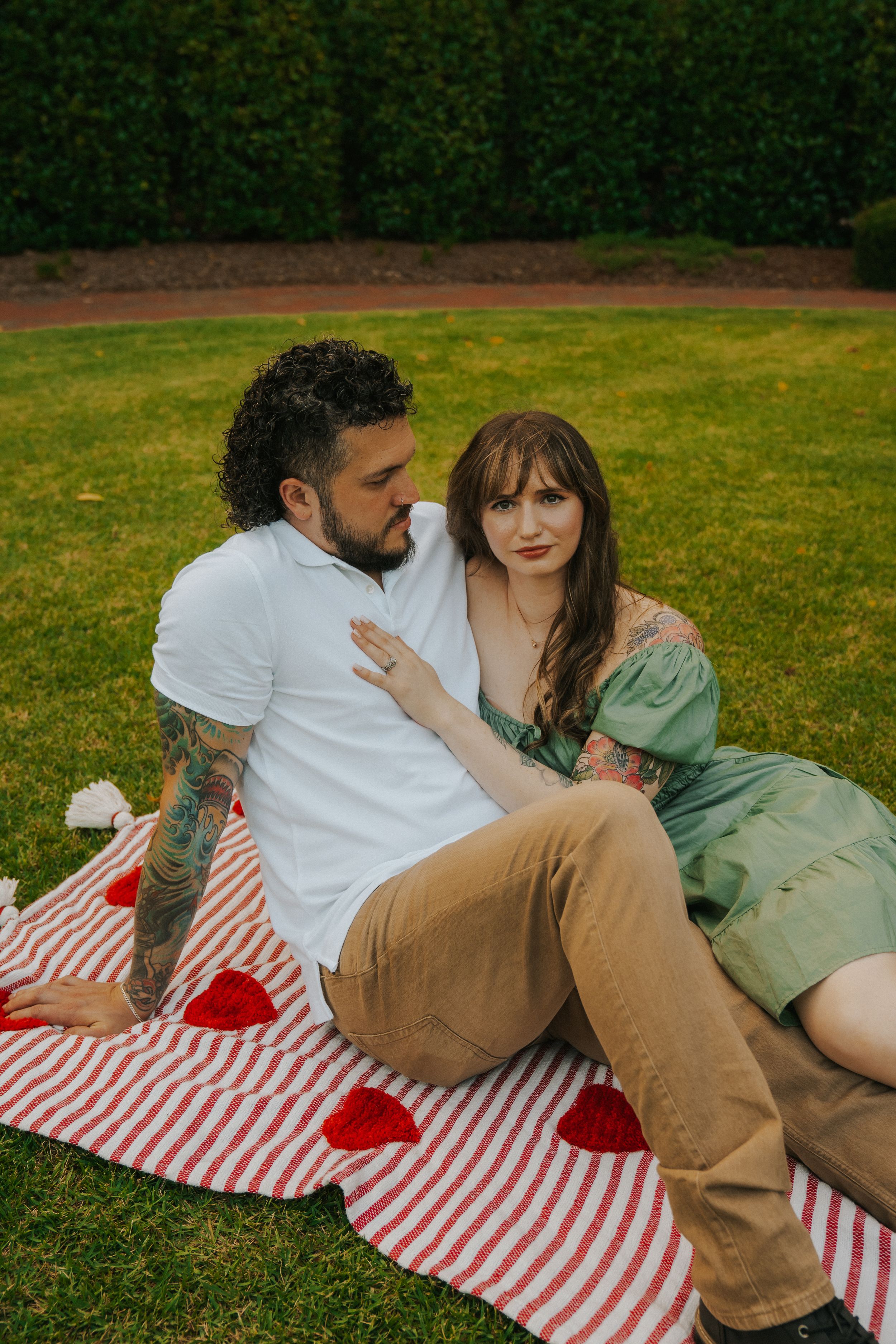 Two people share an intimate moment on a red and white striped blanket in a grassy outdoor setting.