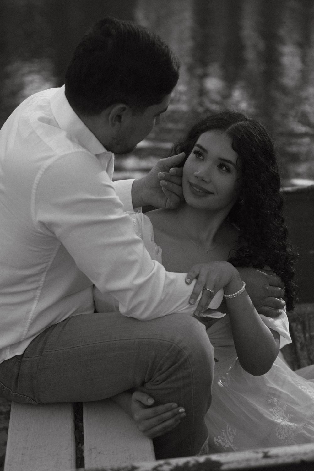 A romantic black and white photo of a couple in formal attire sharing an intimate moment by the water.