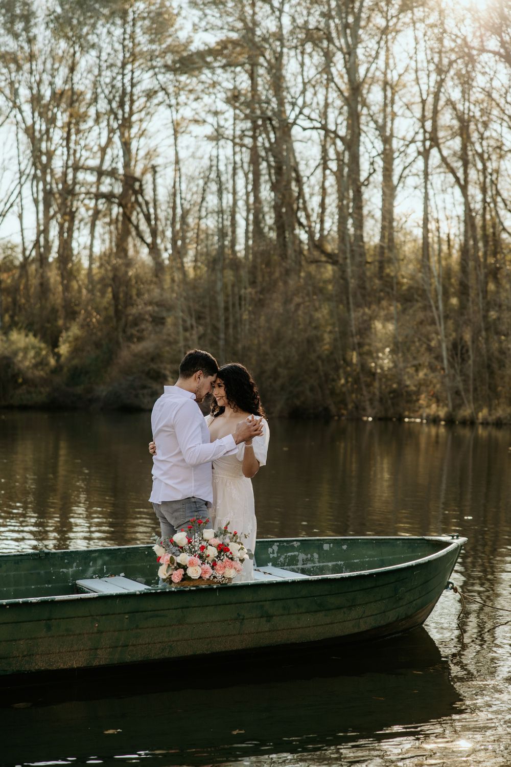 A couple stands intimately in a green rowboat on a tranquil lake surrounded by autumn trees.