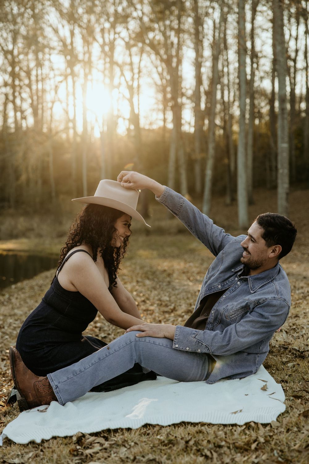 A playful couple having fun on a white blanket in the woods during golden hour sunset.