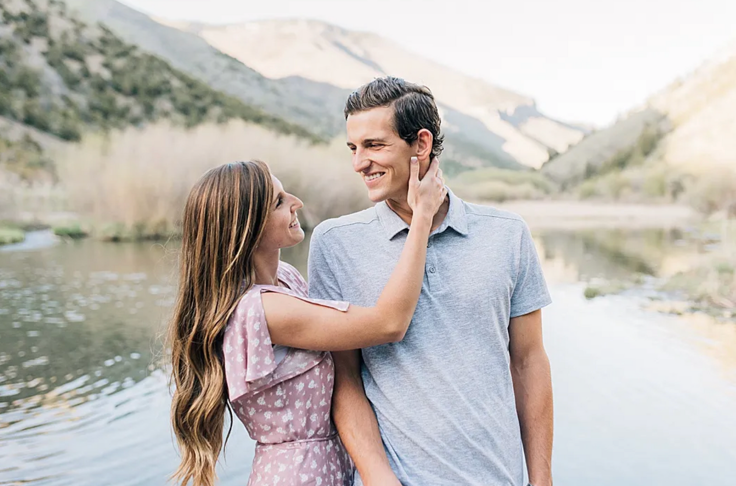 A loving couple shares a tender moment by a scenic mountain lake surrounded by rolling hills.