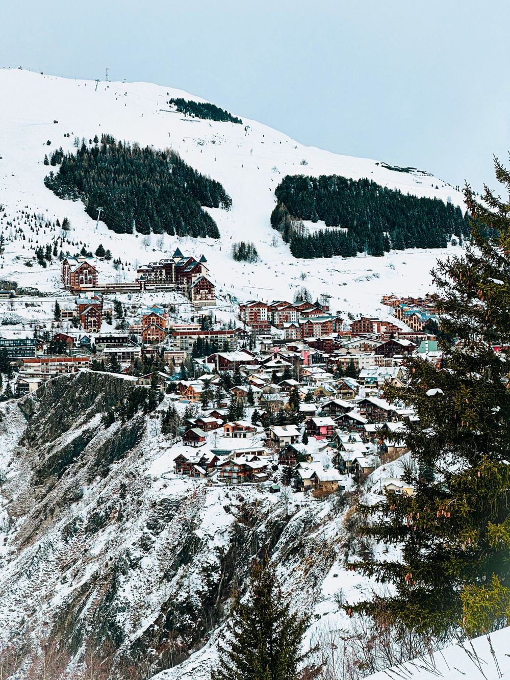 Picturesque alpine village perched on snowy mountainside with ski slopes in background.