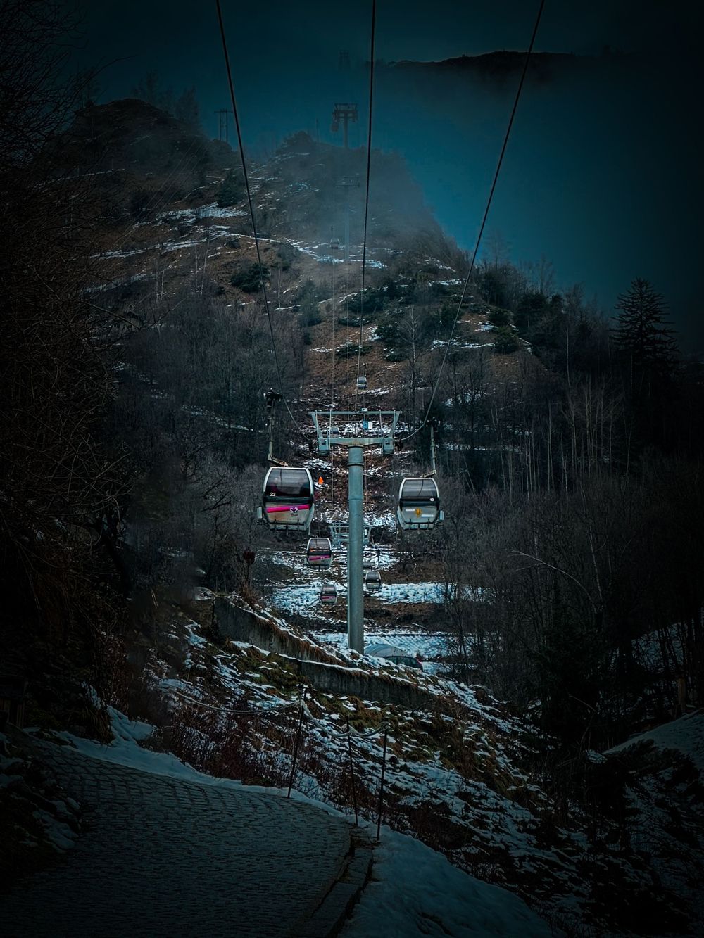 Ski lift gondolas ascending snowy mountain slopes at dusk.
