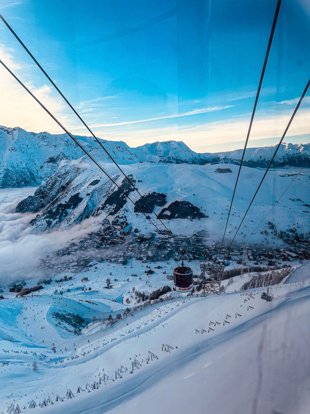 Aerial view of snow-covered mountain resort with cable car lines stretching across blue sky.