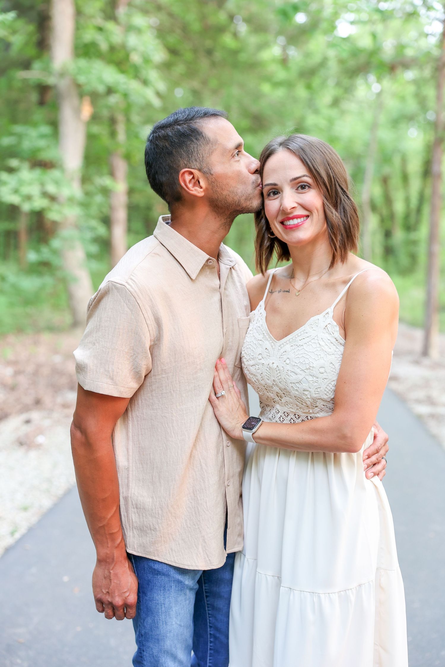 A romantic couple sharing a tender moment on a tree-lined path, with her in a white dress and him in a beige shirt in Branson Missouri.