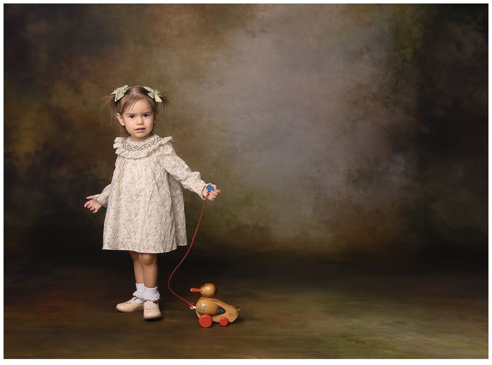 vintage style portrait of newborn girl in heirloom dress pulling a vintage wooden duck toy behind her.