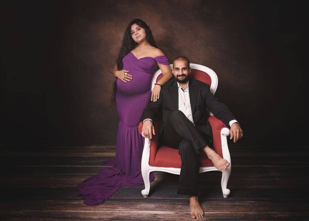 Elegant maternity portrait with couple in formal wear against dark background.