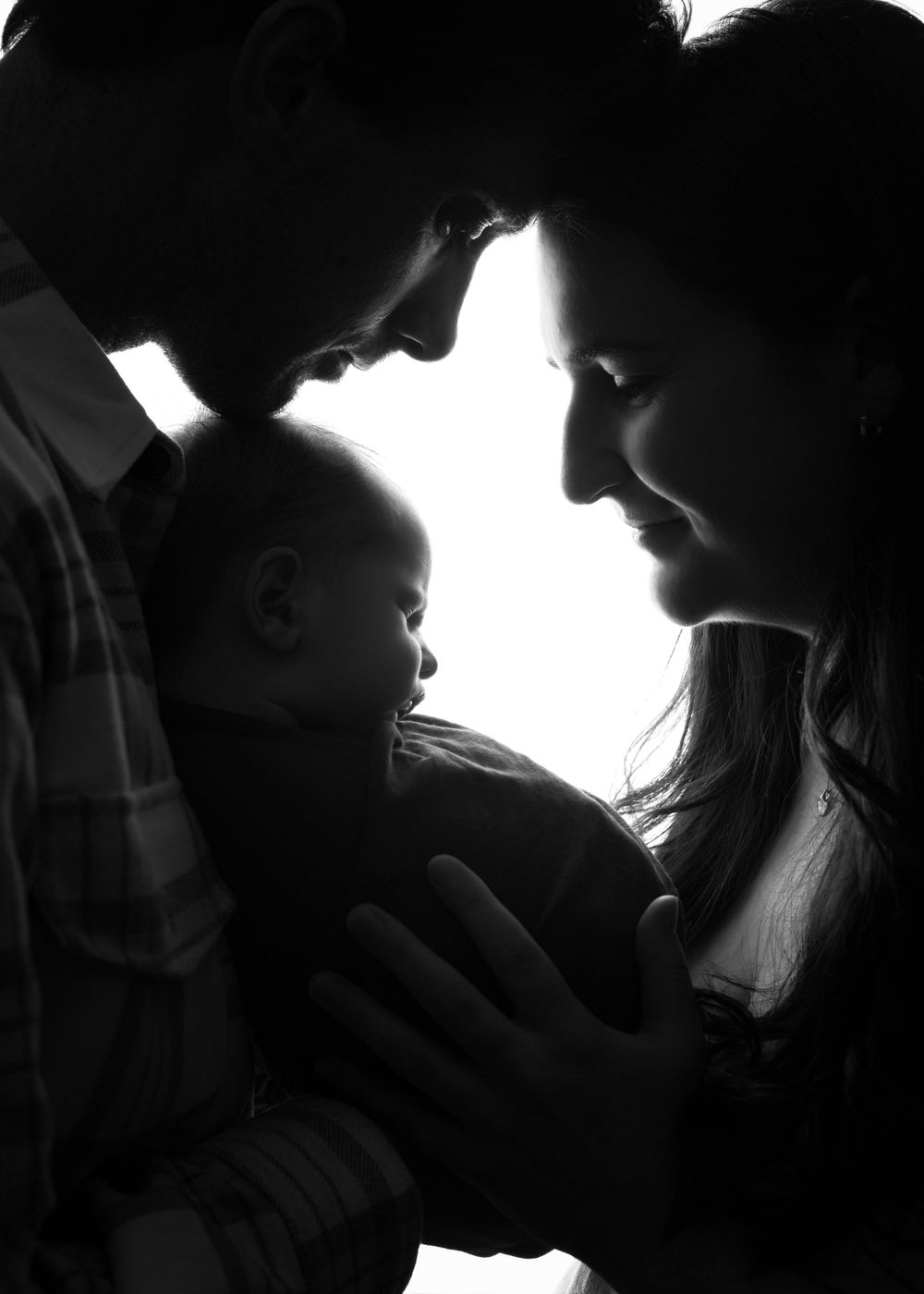 Intimate black and white silhouette of parents with newborn in tender moment.