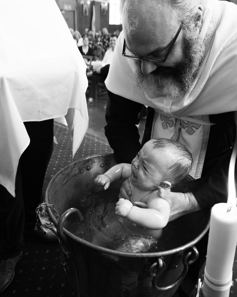 Black and white photograph of a baptism ceremony with a baby being held over a baptismal font.
