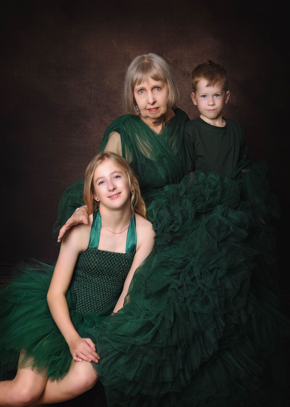 Studio portrait of three people in emerald green formal wear against a dark background.