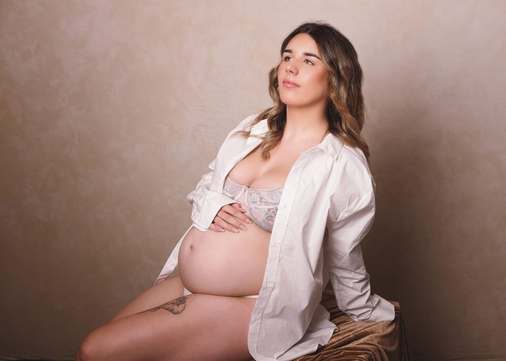 Artistic maternity portrait of an expectant mother wearing white shirt against neutral background.