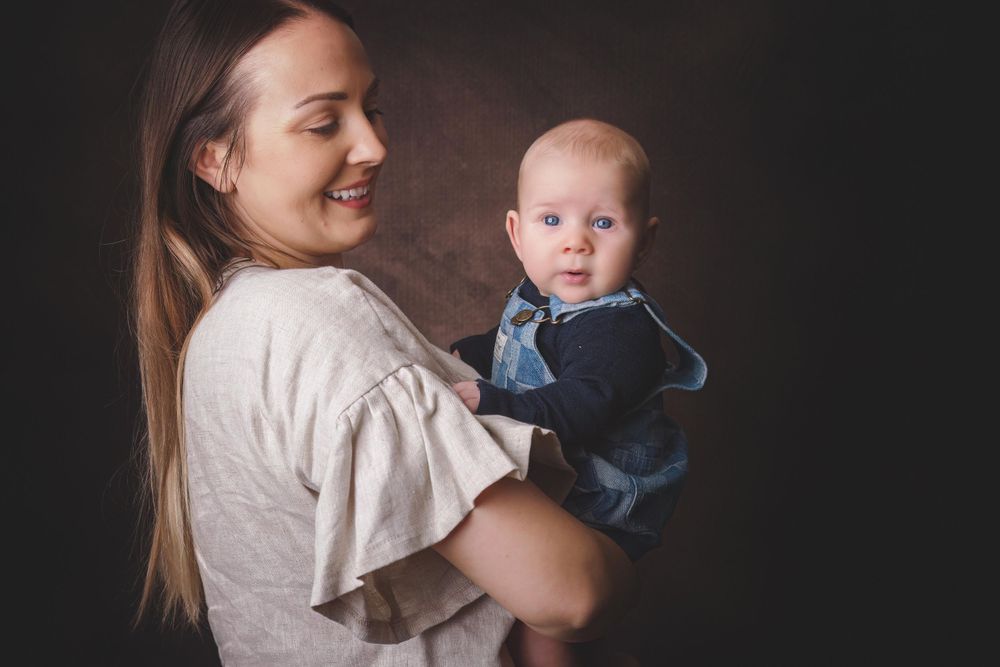 Studio portrait showing joyful interaction between parent and baby against dark background.