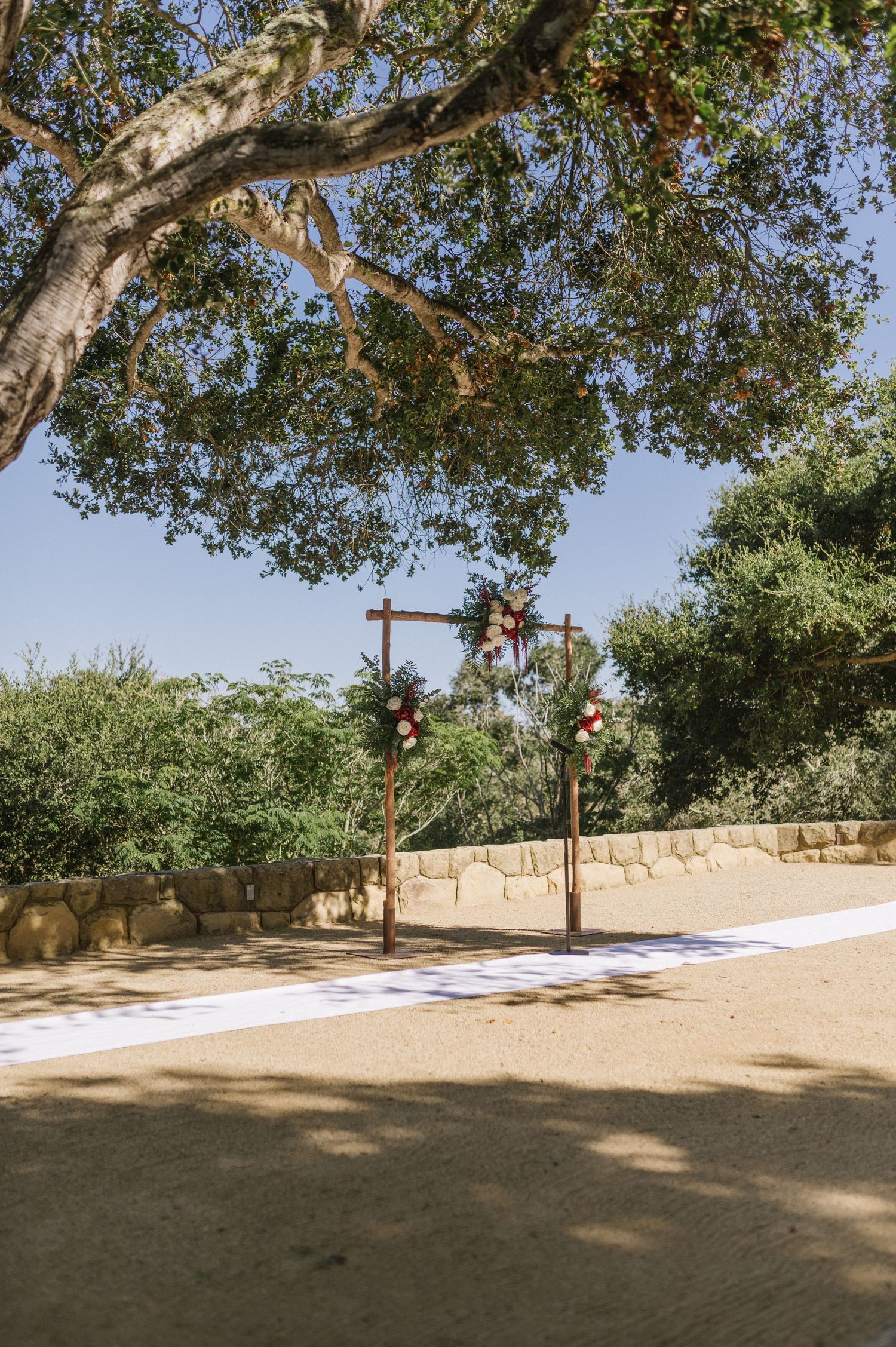 Wooden cross wedding altar setup under a large tree in an outdoor venue.