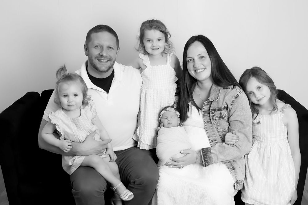 Black and white portrait of a family of six sitting together against a light background.