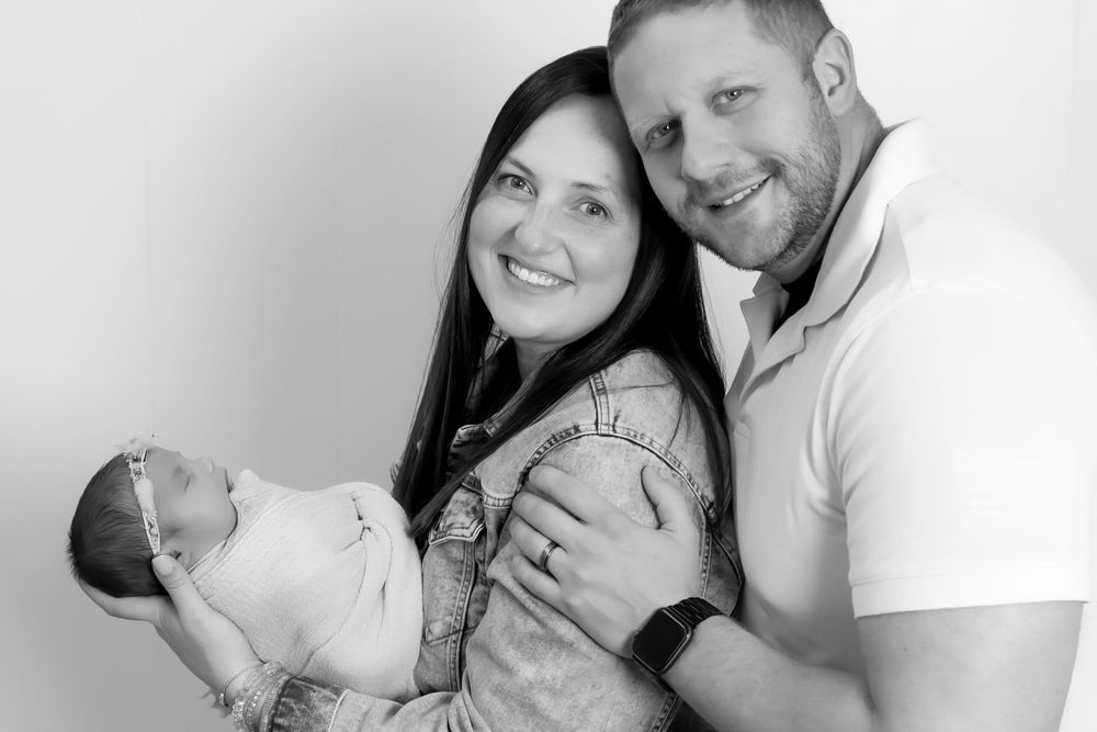 Black and white portrait of parents sharing a tender moment with their newborn baby.