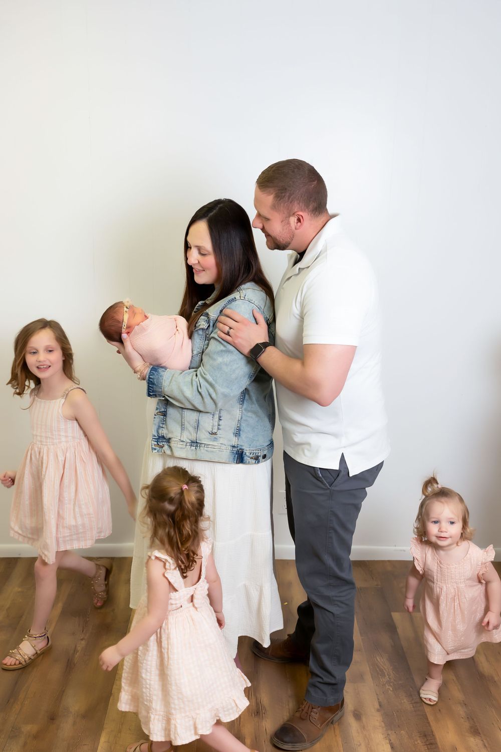 Family group in casual attire standing together on wooden floor, wearing pink dresses and denim.