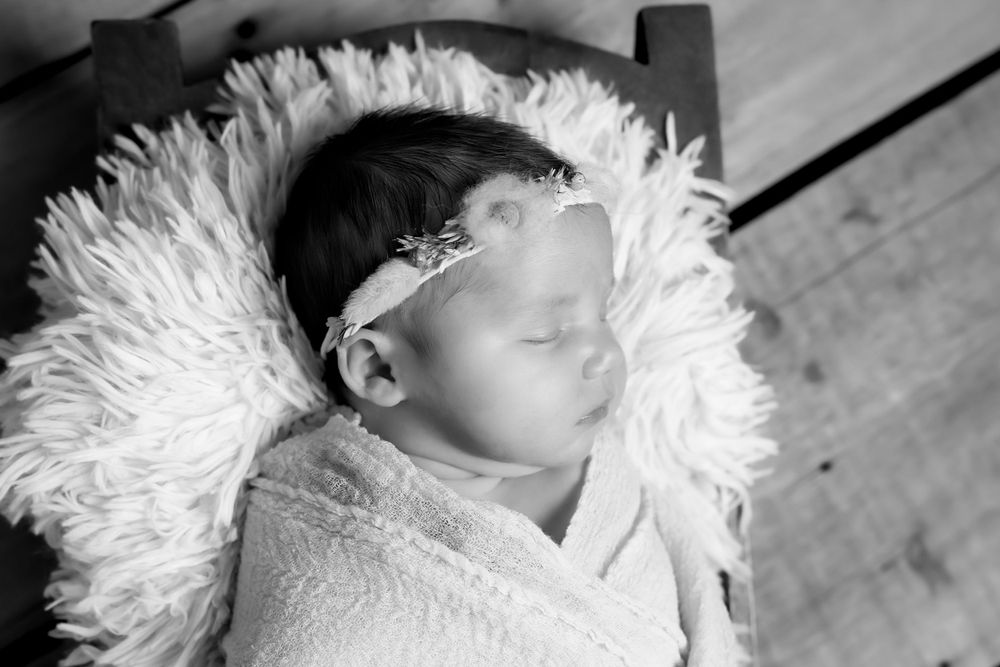 A peaceful sleeping newborn wrapped in white swaddling with a feathery backdrop in black and white photography.